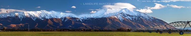 Mount Hutt in winter with farming center pivot in foreground and hot air balloon in sky, Canterbury, New Zealand